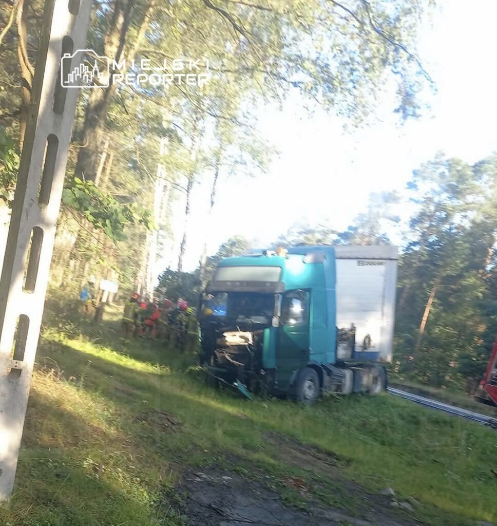 Ciągnik siodłowy z uszkodzoną przednią częścią stoi na poboczu drogi w otoczeniu drzew, obok grupy ratowników.