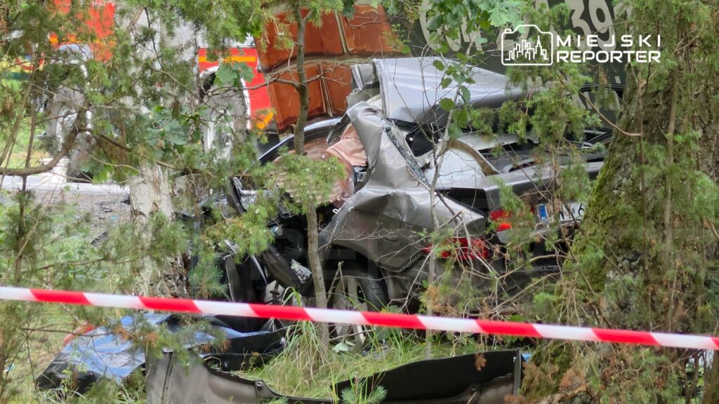 Rozbity samochód osobowy leży w zaroślach, otoczony przez policyjną taśmę zabezpieczającą.