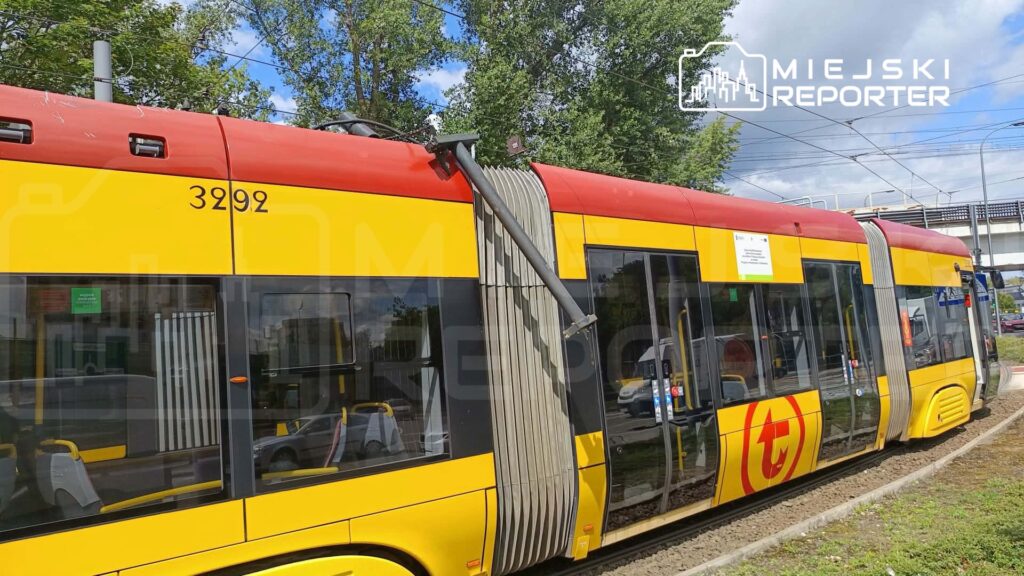 Tramwaj w żółto-czerwonych barwach zatrzymany na przystanku, z widocznymi numerem 3292 i otoczeniem z zielenią.