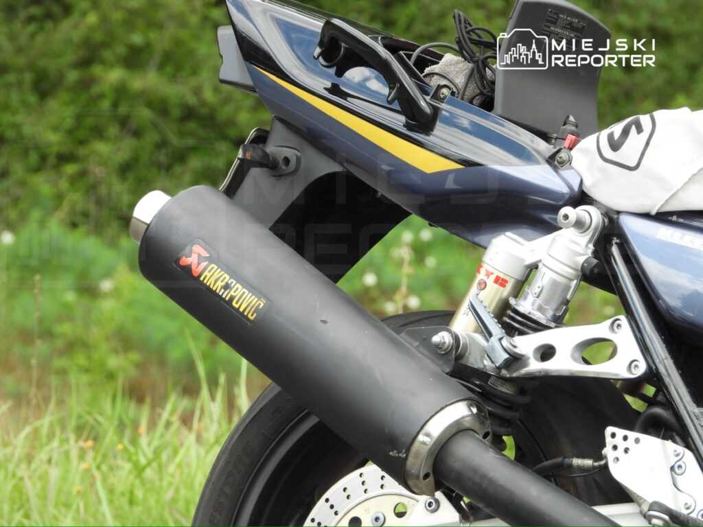 Motocykl z widocznym tłumikiem Akrapovič w otoczeniu zieleni.