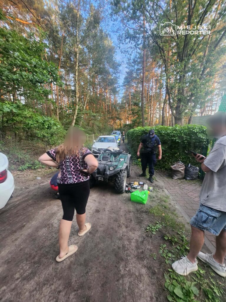Kobieta z długimi włosami stoi z rękami w biodrach obok quada, a obok niej mężczyzna w mundurze policyjnym sprawdza otoczenie.