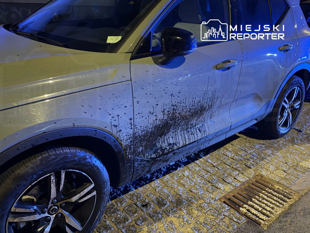 Brudna strona SUV-a z widocznymi plamami błota, zaparkowanego na kostkowanej nawierzchni w nocy.