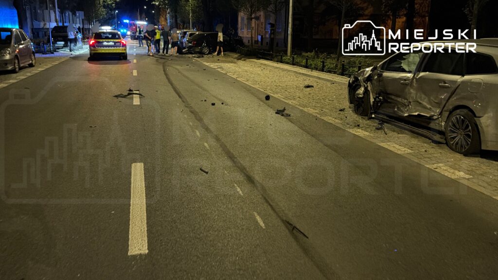 Na ulicy widoczne ślady hamowania oraz uszkodzone pojazdy, obok grupka ludzi i służby ratunkowe.