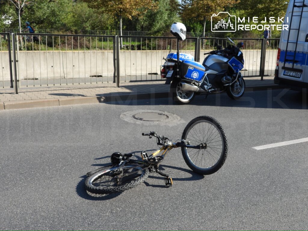 Rower leży na jezdni obok policyjnych motocykli, w tle widać rowerzystów na chodniku.