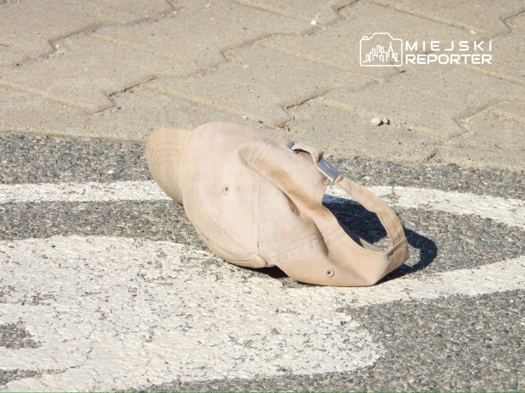 Czapka leży na pasie drogowym obok białej linii na asfaltowej nawierzchni.