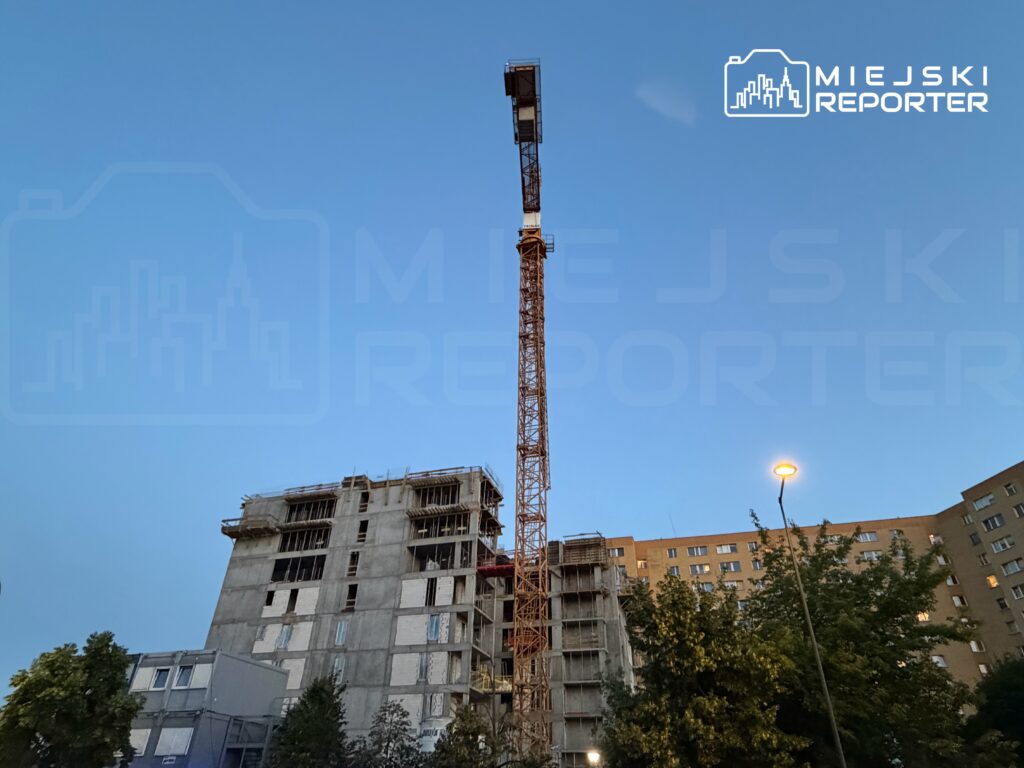 Dźwig budowlany pracujący przy wznoszeniu nowego, betonowego budynku mieszkalnego w miejskim otoczeniu.