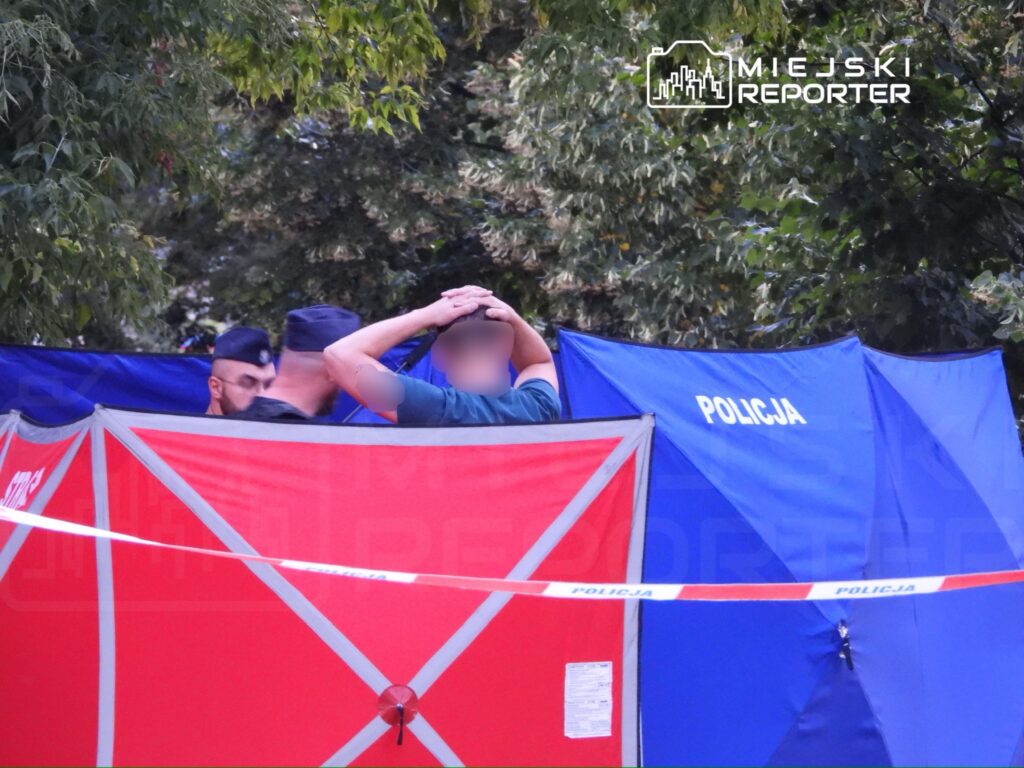 Grupa policjantów rozmawia w pobliżu niebieskich i czerwonych namiotów zabezpieczających miejsce zdarzenia.