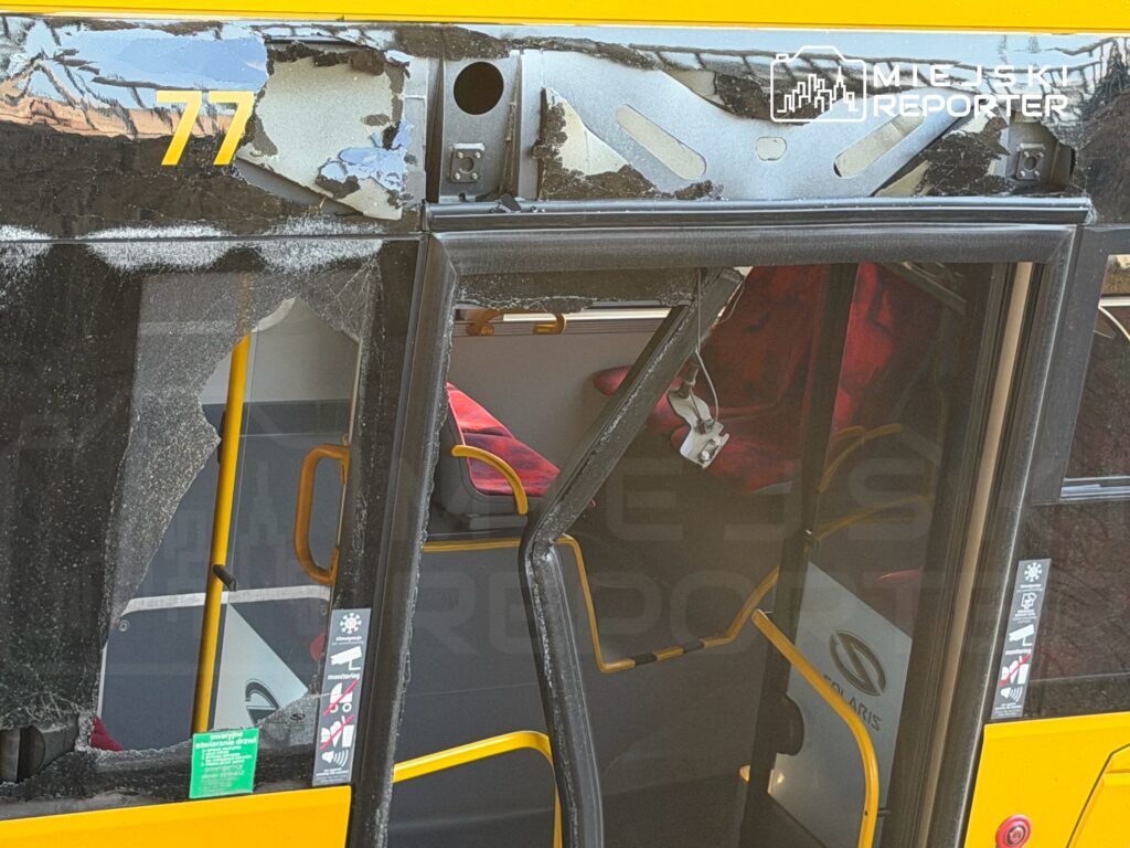 Zniszczony przód autobusu miejskiego z numerem 77, z uszkodzoną szybą i widocznymi wnętrzami pojazdu.
