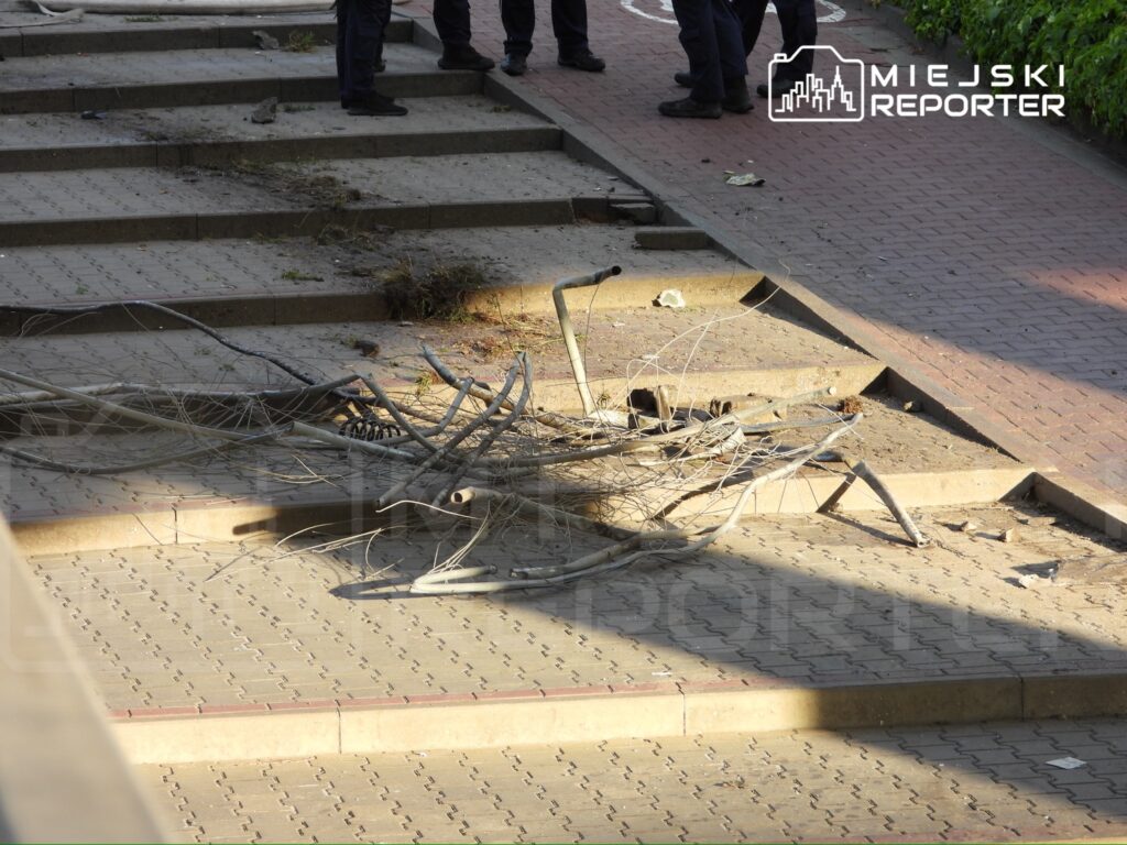 Złamane metalowe pręty leżą na schodach, obok grupy policjantów w mundurach.