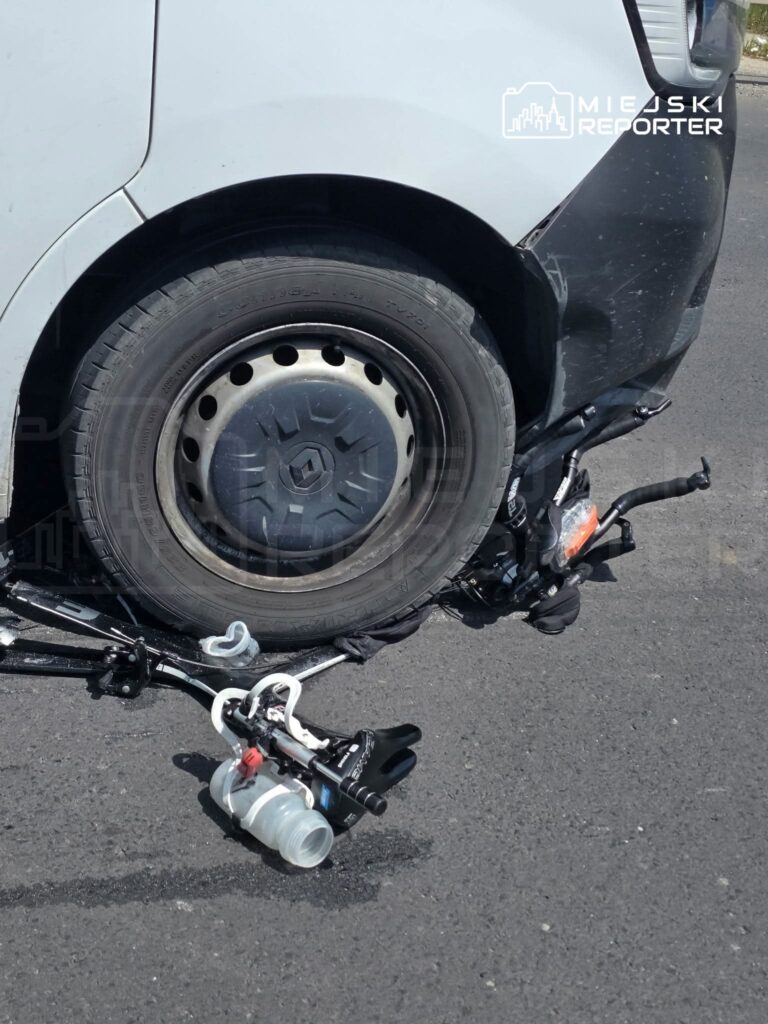 Uszkodzone koło samochodu osobowego leży na asfalcie obok odłączonego mechanizmu.