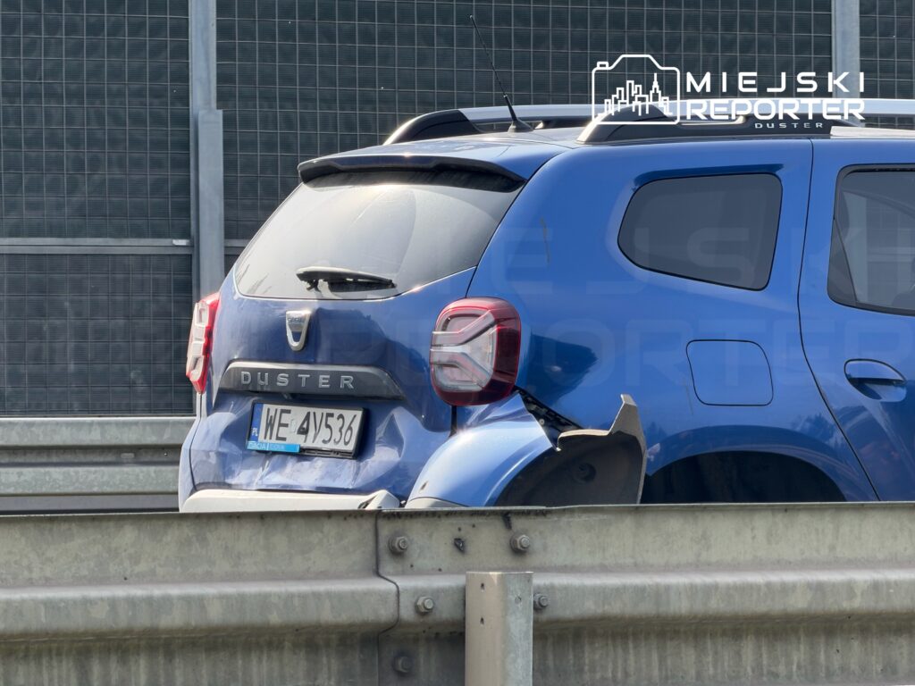 Niebieski samochód osobowy Dacia Duster z uszkodzoną tylną częścią stojący na pasie drogowym.