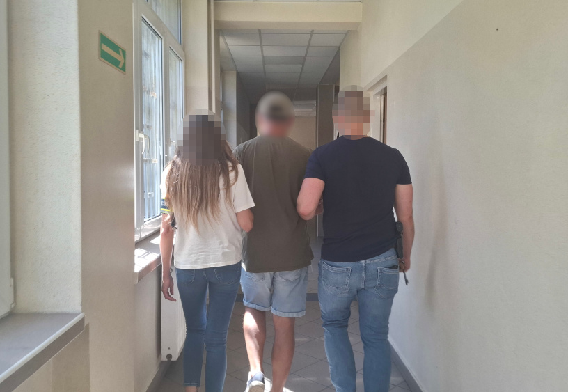 Trzy osoby idą korytarzem w budynku, jedna z nich trzyma rękę na ramieniu innej.