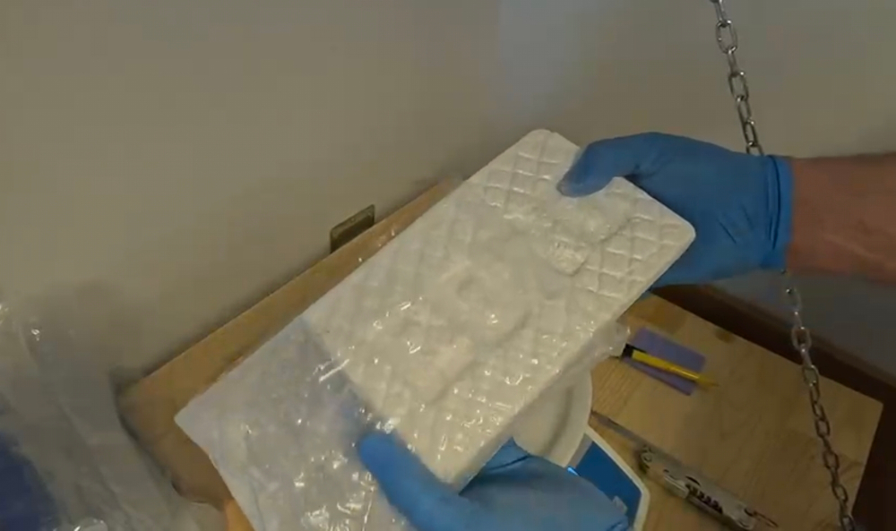 Mężczyzna w niebieskich rękawiczkach trzyma plastikową formę z wytłoczonym wzorem w jasnym otoczeniu.