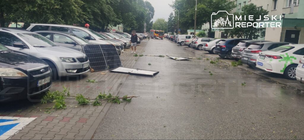 Na ulicy leżą uszkodzone panele słoneczne, a obok przechodzi mężczyzna z gałęziami w rękach.