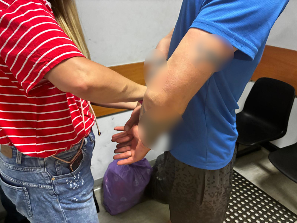 Kobieta w czerwono-białą kratkę zakłada ręce mężczyźnie w niebieskiej koszulce na plecach. W tle widać plastikowe krzesła.