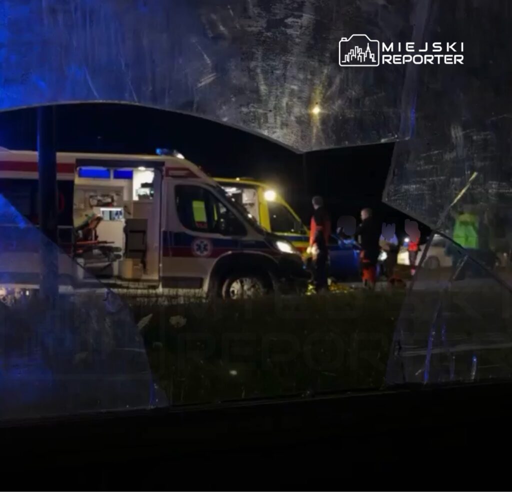 Zespół ratowników medycznych pracuje przy wypadku drogowym, obok ambulansu na oświetlonej drodze nocą.