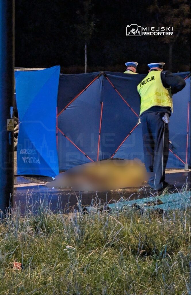 Policjanci zabezpieczają miejsce zdarzenia, otaczając je niebieskim namiotem, w nocy na ulicy.