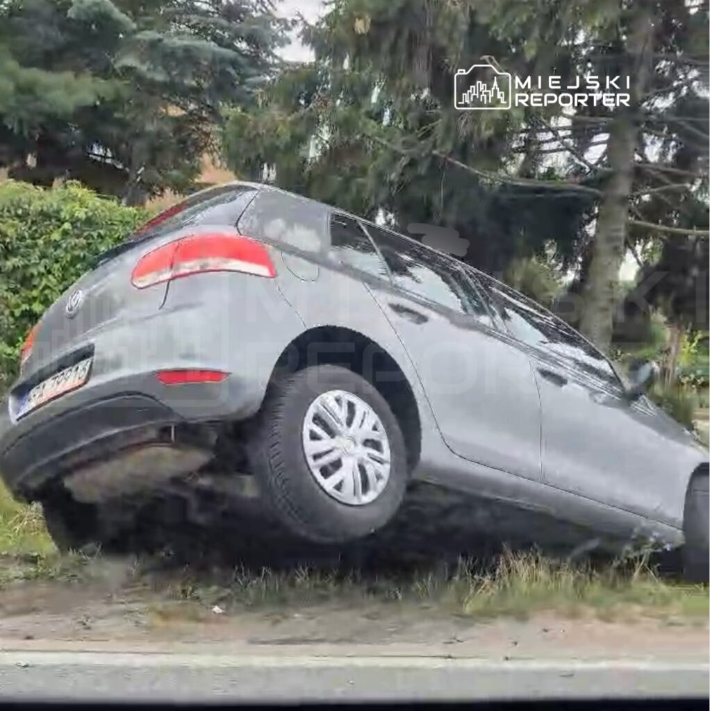 Samochód osobowy marki Volkswagen stoi na poboczu drogi, uniesiony na jednym z kół, z otaczającą zielenią w tle.