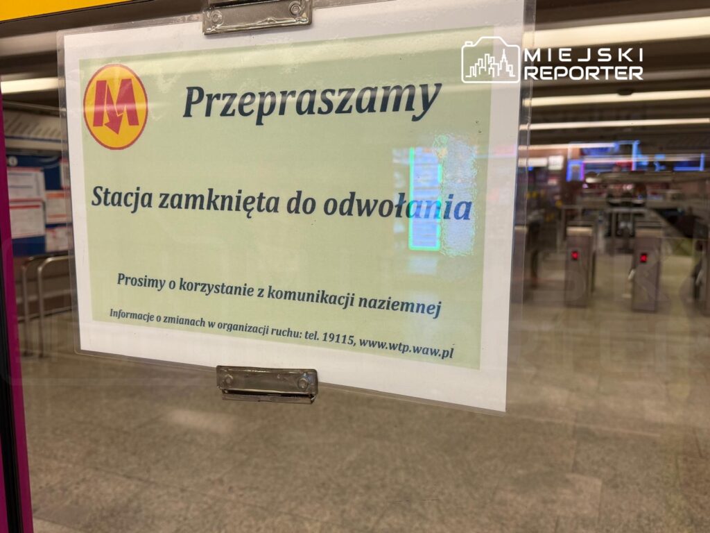 Tablica informacyjna w kolorze zielonym z napisem "Przepraszamy, Stacja zamknięta do odwołania" zawieszona przy wejściu do stacji metra.