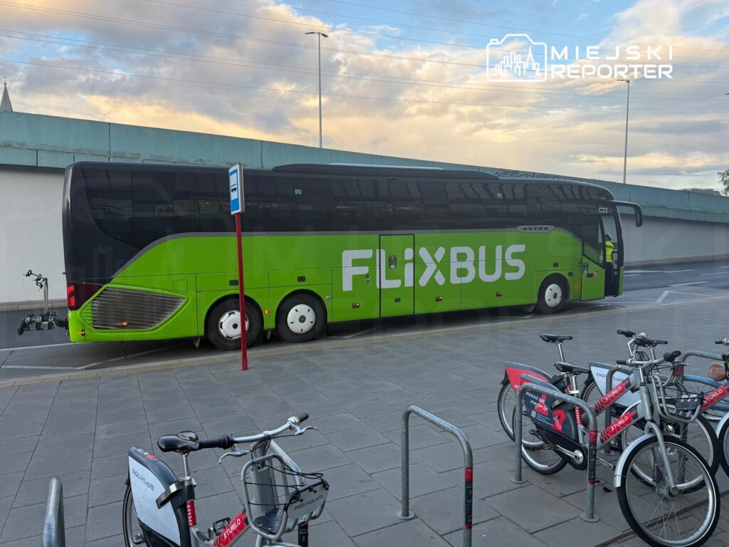 Zielony autobus FlixBus zatrzymany na przystanku, w tle rząd rowerów miejskich.