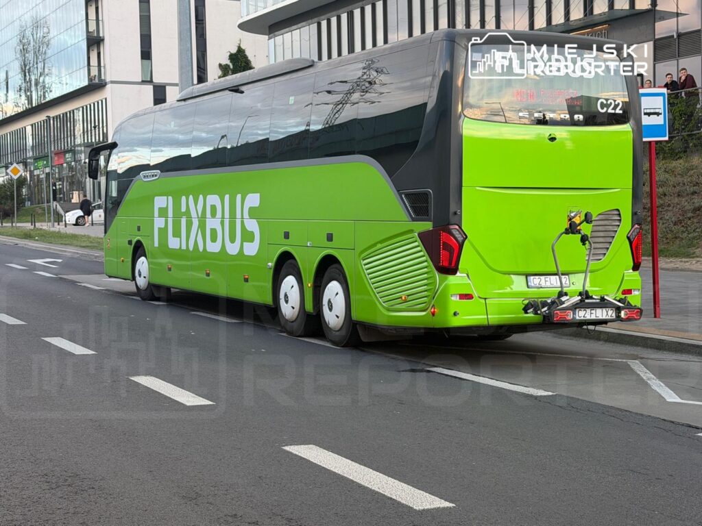 Zielony autobus FlixBus zatrzymany na przystanku, obok nowoczesny budynek biurowy.