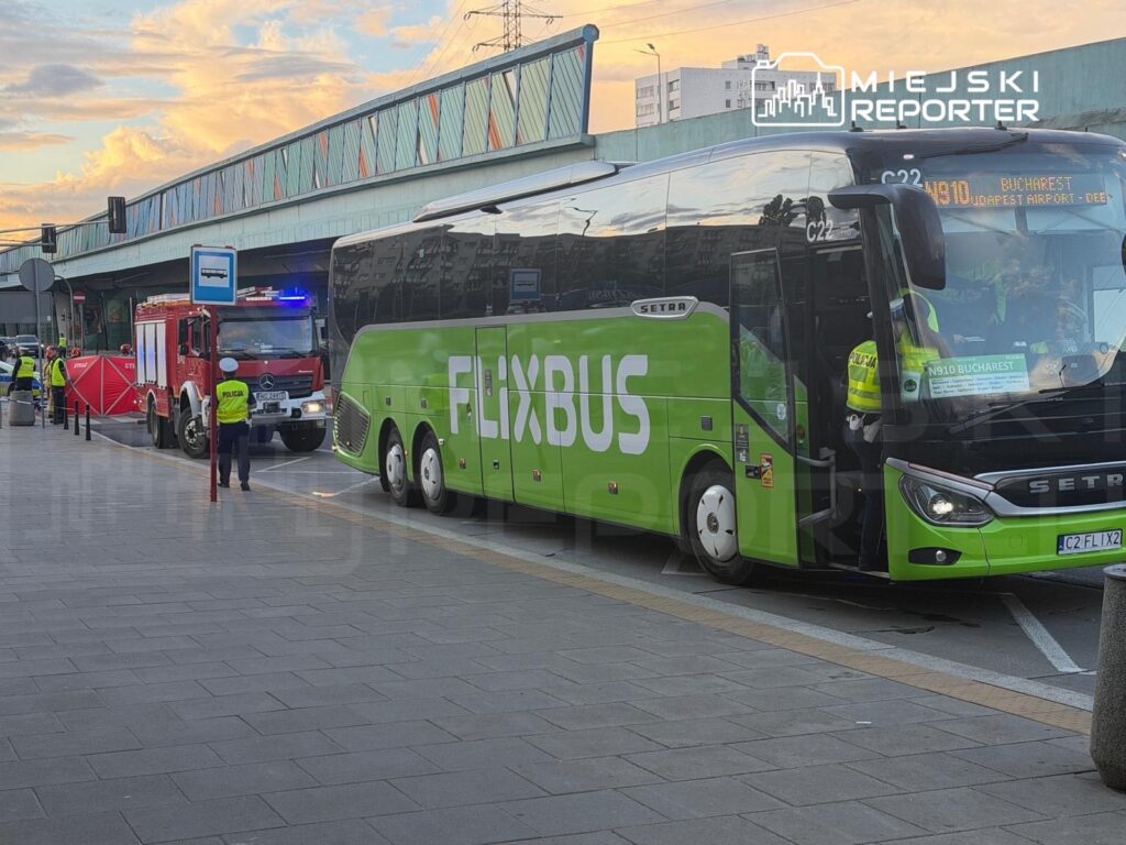 Zielony autobus FlixBus zatrzymany na przystanku, obok wozu strażackiego i policjanta kierującego ruchem.