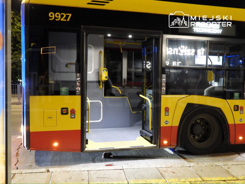 Autobus miejski z otwartymi drzwiami stoi na przystanku, oświetlony nocnym światłem.