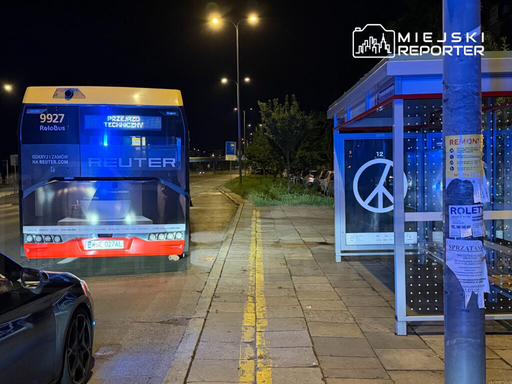 Autobus z napisem "PRZEJAZD TECHNICZNY" stoi na nocnej ulicy obok przystanku z symbolem pokoju.