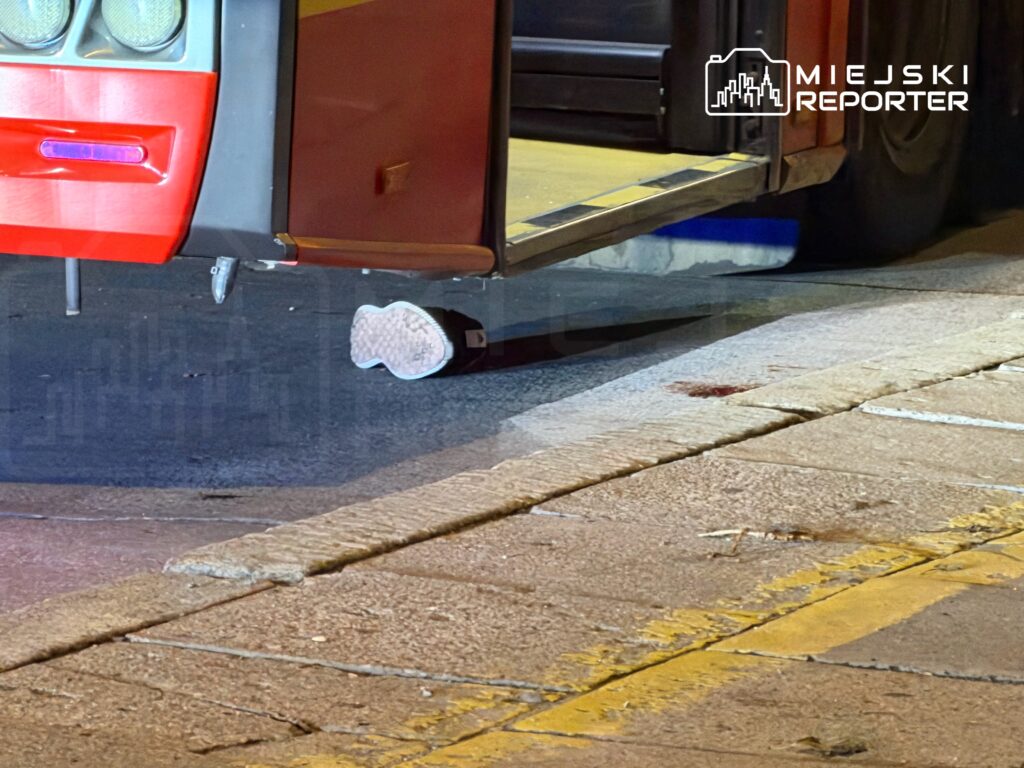 Autobus z opuszczonymi schodkami stoi na przystanku, a na chodniku widać odciśniętą stopę.