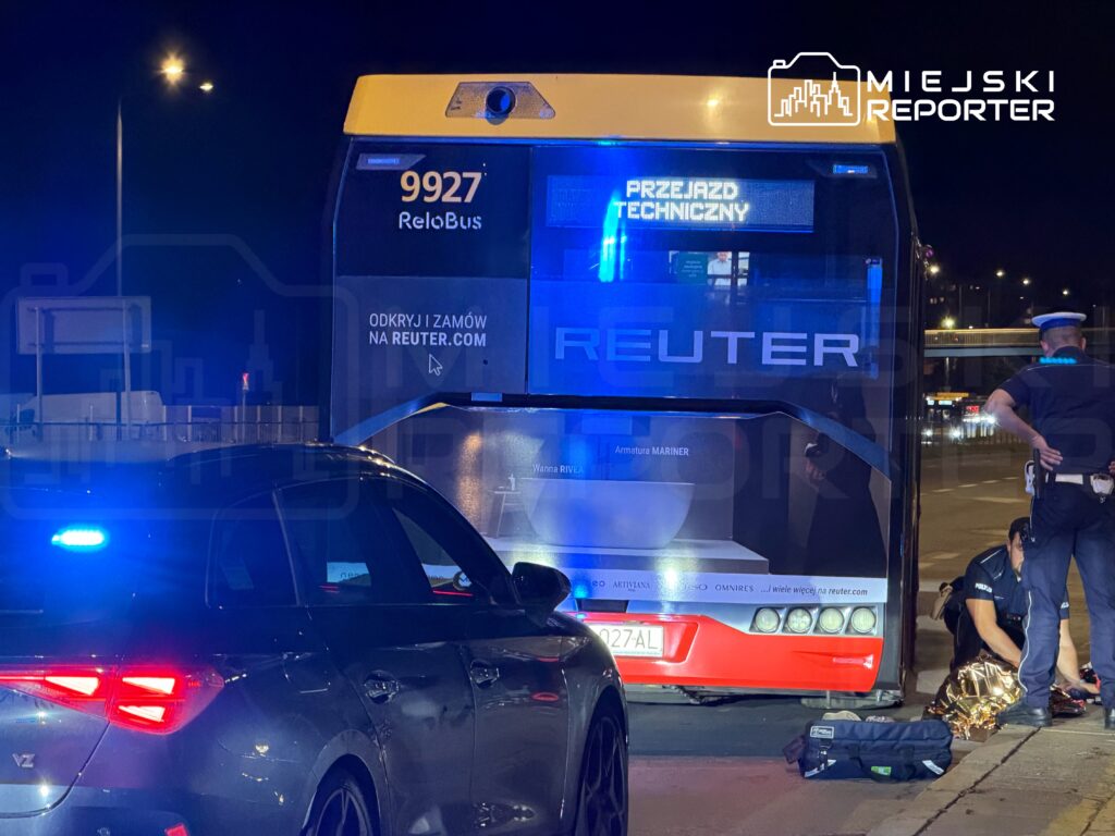 Policyjny radiowóz z niebieskimi światłami stoi obok autobusu ReloBus, przy którym pracują funkcjonariusze. Na wyświetlaczu autobusu widnieje napis "PRZEJAZD TECHNICZNY".