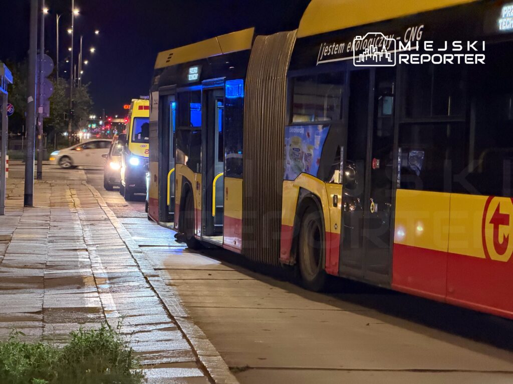 Autobus przystanek w nocy, z włączonymi światłami, obok przejeżdżający samochód. Na autobusie widoczny napis "Jestem ekologicznym CNG".