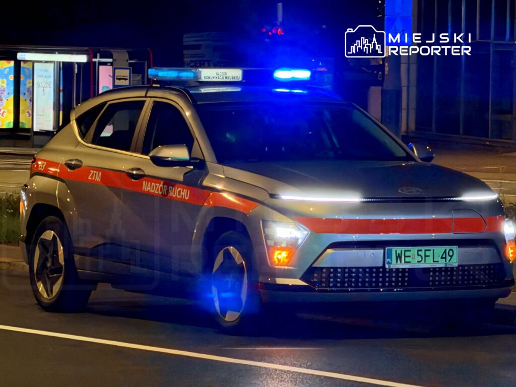 Samochód z oznaczeniem "ZTM Nadzór Ruchu" stoi na drodze, oświetlony niebieskimi światłami policyjnymi.