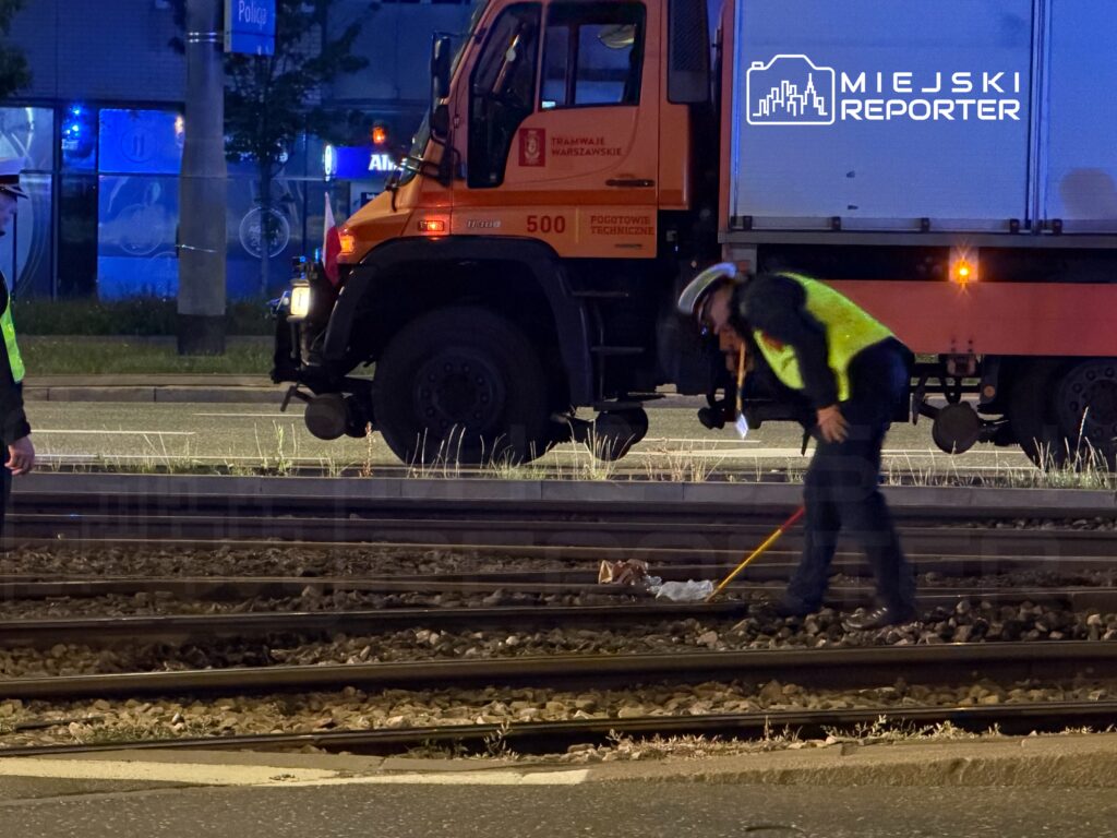 Funkcjonariusz w kamizelce odblaskowej bada torowisko w pobliżu zaparkowanego pojazdu technicznego.