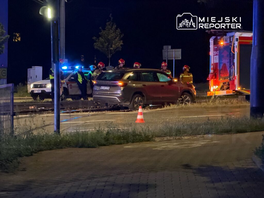 Grupa ratowników i policjantów w kamizelkach odblaskowych prowadzi działania na miejscu wypadku drogowego w nocy.