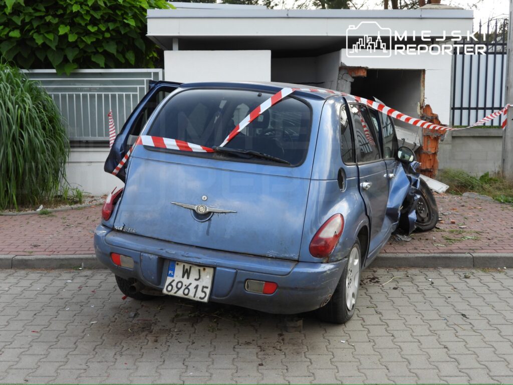 Nieoznakowany niebieski samochód zaparkowany na chodniku, z uszkodzeniami tyłu, obok zniszczona ściana budynku.