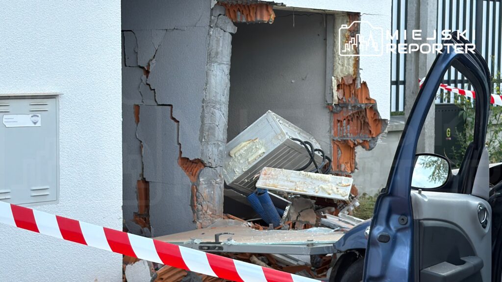 Uszkodzona ściana budynku z wyłamaną częścią, w której znajduje się uszkodzony sprzęt AGD, ogrodzona taśmą ostrzegawczą.