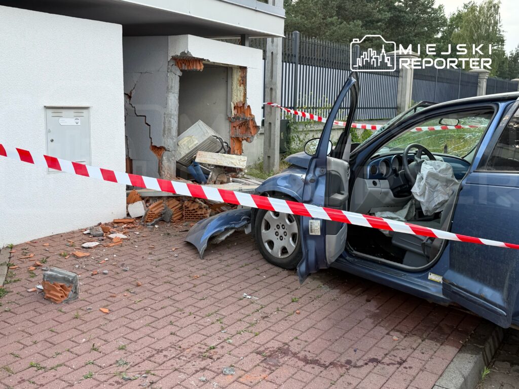 Niebieski samochód z otwartymi drzwiami stoi na chodniku obok uszkodzonej ściany budynku, otoczony taśmą ostrzegawczą.