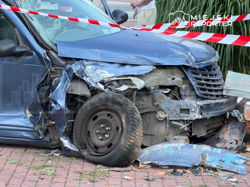 Zniszczony samochód osobowy z wgniecioną karoserią i uszkodzoną przednią częścią, otoczony taśmą zabezpieczającą.