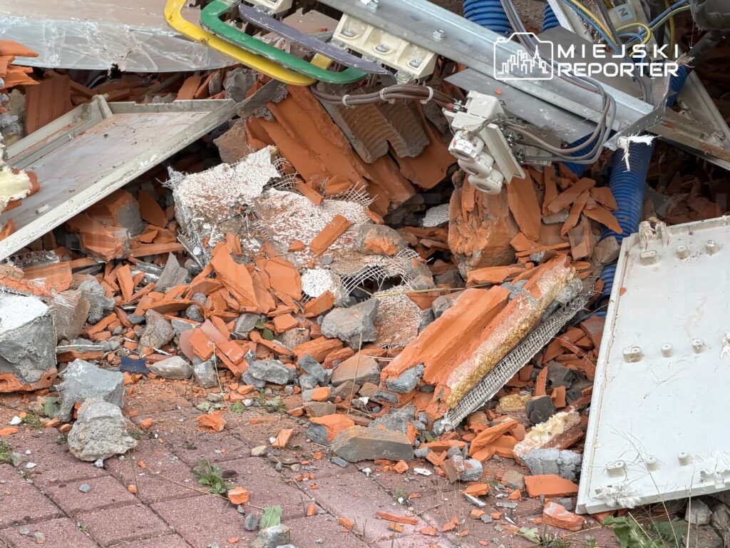 Zniszczone fragmenty budynku, w tym cegły i beton, leżą na ziemi obok metalowych elementów konstrukcyjnych.