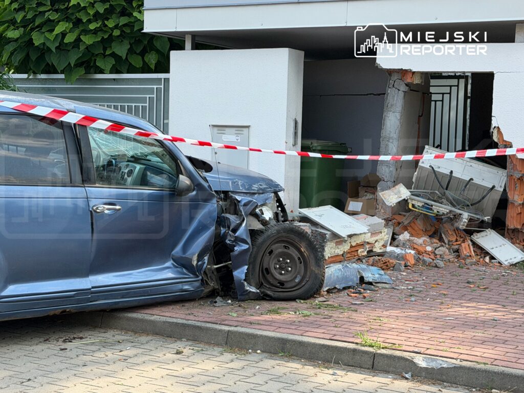 Samochód osobowy z uszkodzoną przednią częścią stoi obok zniszczonego muru budynku, otoczonego taśmą ostrzegawczą.