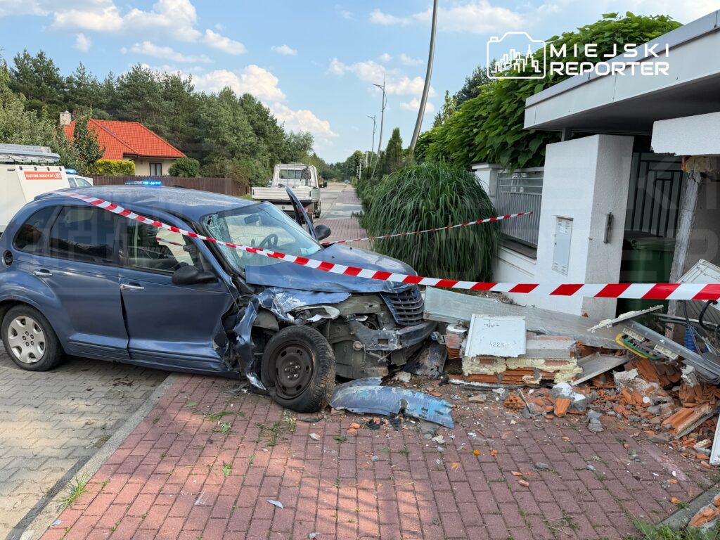 Uszkodzony niebieski samochód osobowy stoi na chodniku obok zniszczonego muru, zabezpieczony taśmą ostrzegawczą.