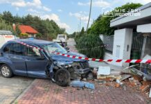 Uszkodzony niebieski samochód osobowy stoi na chodniku obok zniszczonego muru, zabezpieczony taśmą ostrzegawczą.