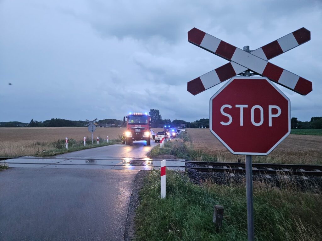 Zespół ratunkowy z włączonymi sygnałami świetlnymi zatrzymany przy przejeździe kolejowym, obok znaku stop.