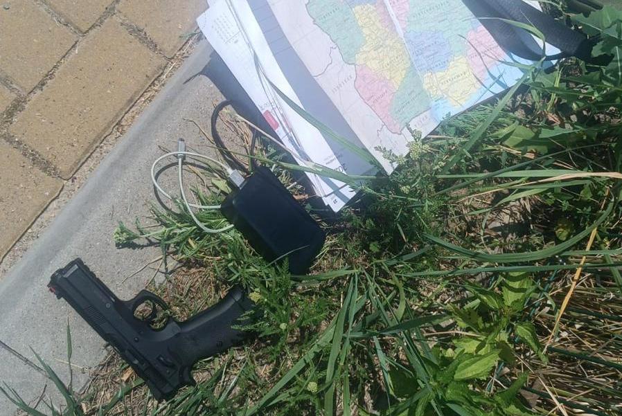 Pistolet leżący na trawie obok mapy i ładowarki, na tle chodnika.