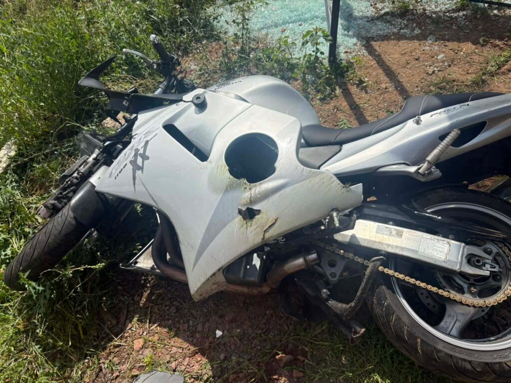 Uszkodzony motocykl leży na trawie, z widocznym otworem w nadwoziu i zarysowaniami na powierzchni.