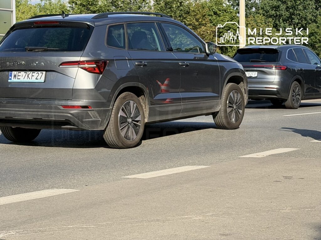 Czarny SUV porusza się po jezdni, obok inny samochód na tle zieleni.