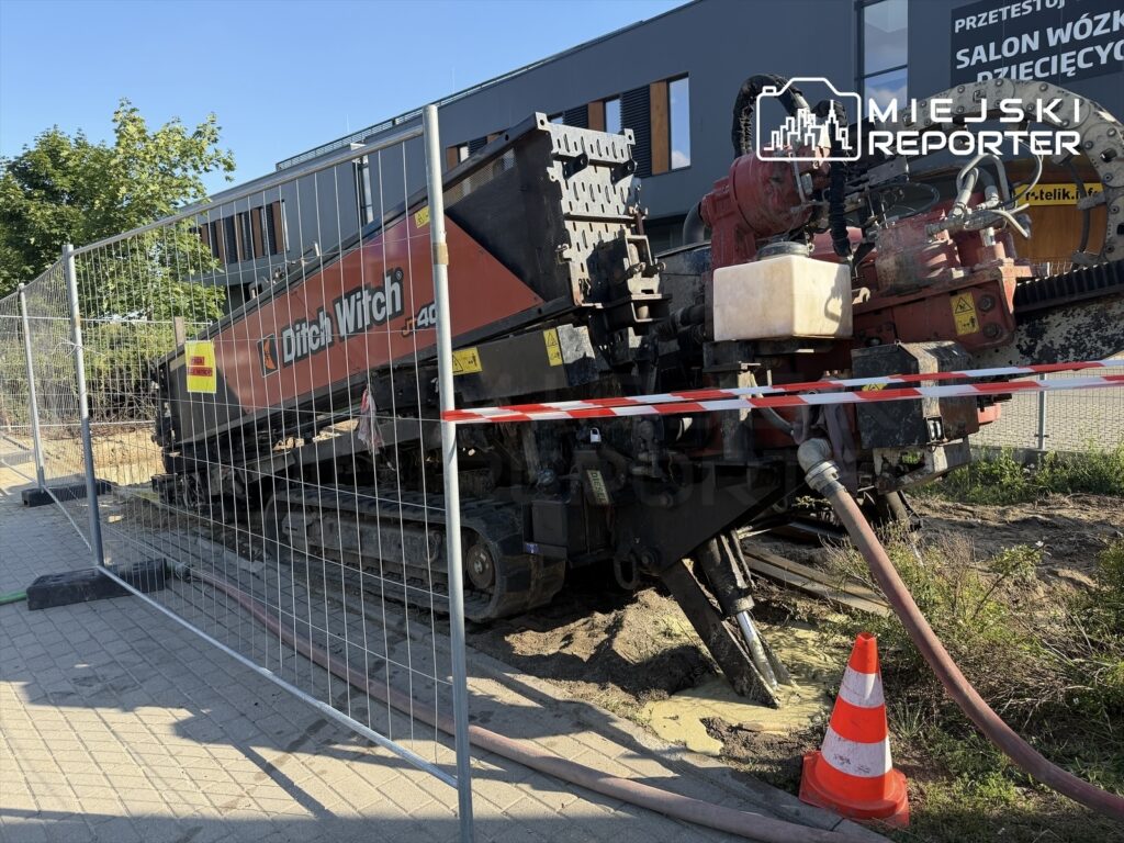 Maszyna budowlana marki Ditch Witch wykonująca prace ziemne na terenie budowy, otoczona ogrodzeniem i taśmą ostrzegawczą.