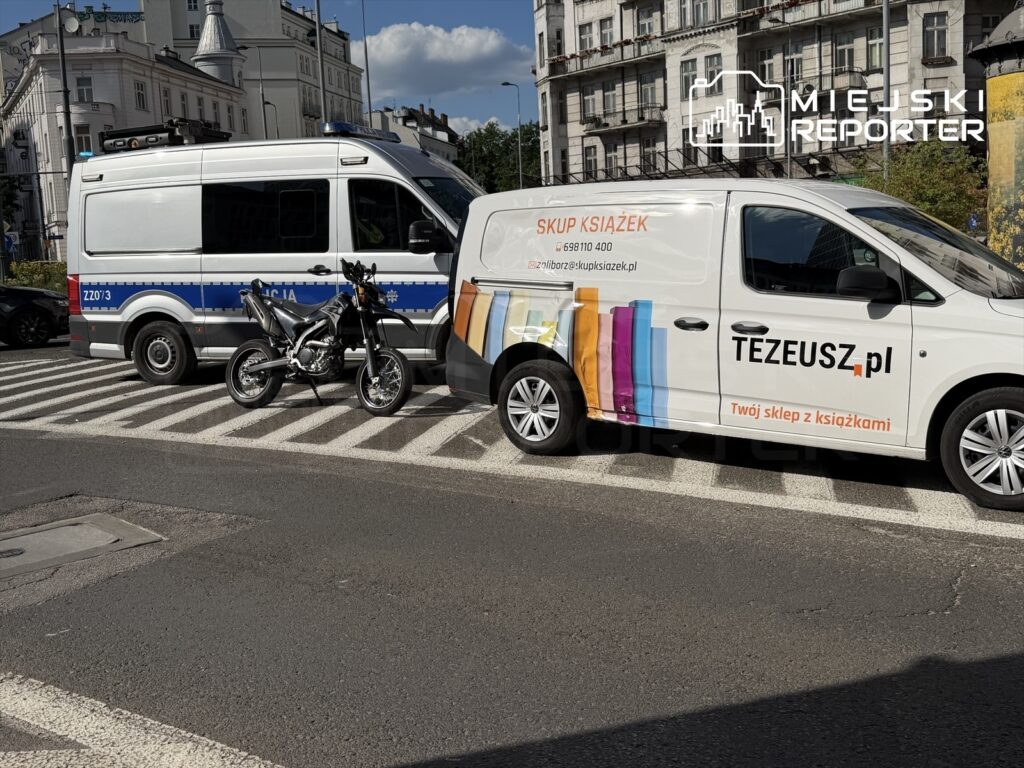 Motocyklista stoi obok radiowozu policyjnego na pasach w pobliżu Placu Unii, obok furgonetki ze sklepem z książkami.