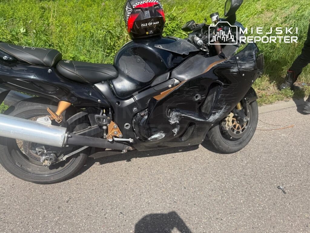Czarny motocykl z uszkodzeniami stoi na drodze, obok widoczny jest fragment trawnika oraz narzędzia.