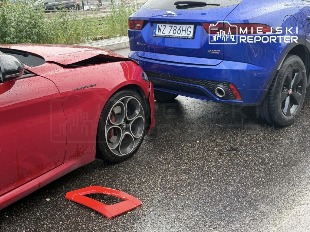 Czerwony sportowy samochód z uszkodzoną karoserią stoi obok niebieskiego SUV-a na mokrej nawierzchni.